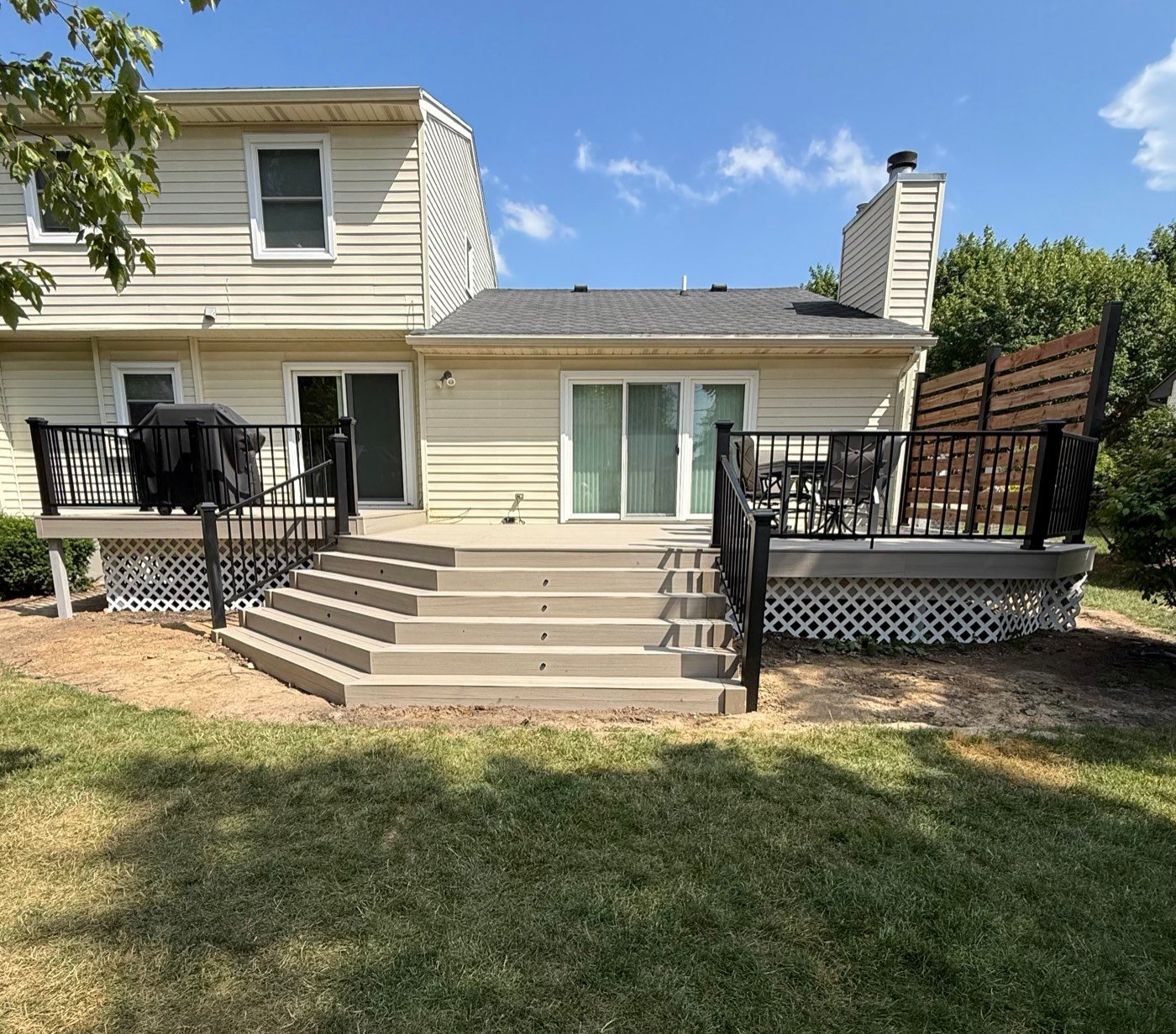 Finished composite deck with wide steps and black railing behind a two-story home